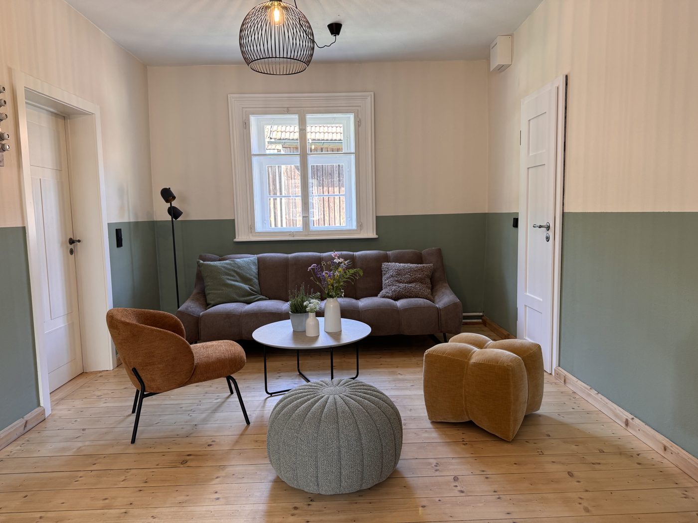 Gemütlicher Raum in der Neuen Effeltermühle mit Sofa, Sessel, Sitzkissen und Blumen vor einem Sprossenfenster